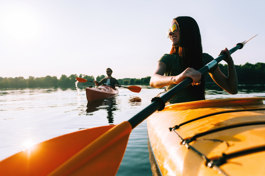Man and woman in single yellow and orange kayaks smiling as they paddle across water. 