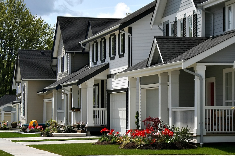 Row of new houses with neutral siding, light landscaping and mature trees around. 