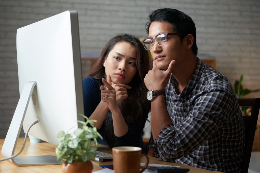 Couple looking thoughtfully at computer. Man is resting his head in his hand and woman is pointing at the screen.