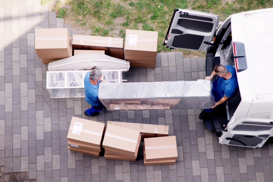 Aerial view of movers in blue uniforms loading boxes and furniture into white van.