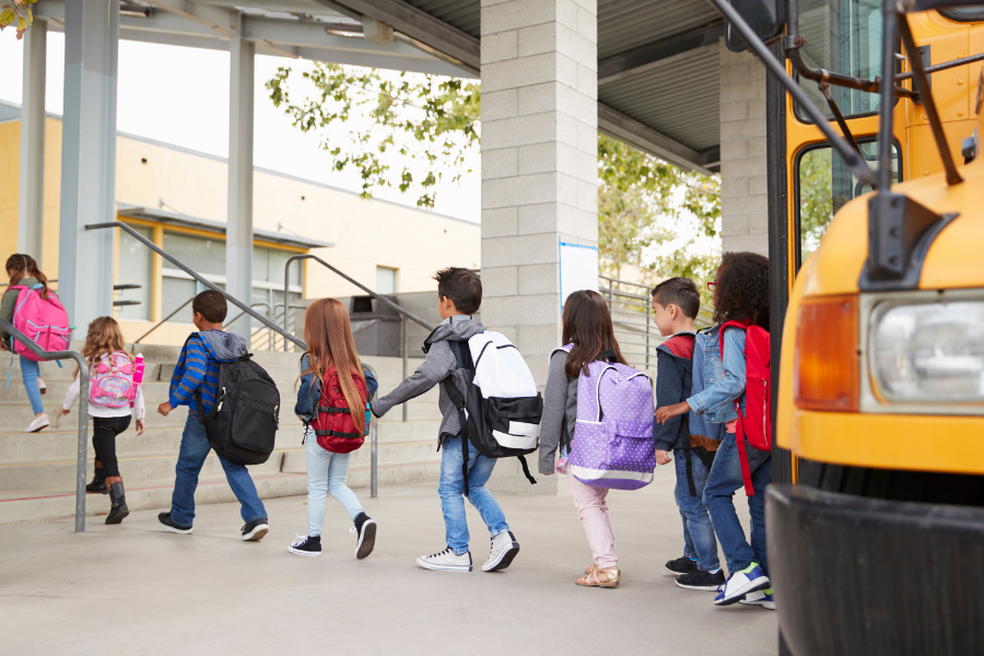 Kids wearing backpacks exit bus into school in a single-file line