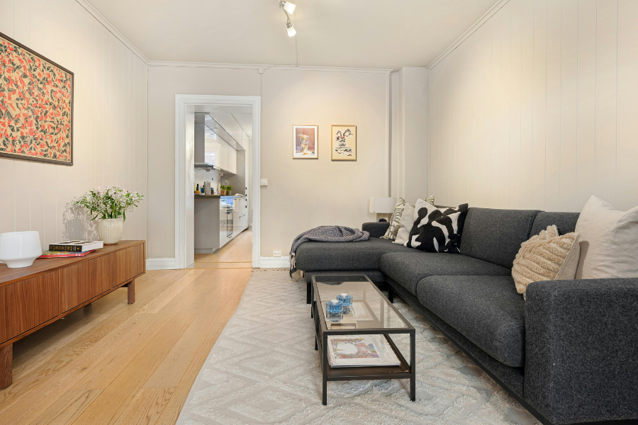 Living room with beige walls and gray couch with three walls in view that make it feel narrow and small. 