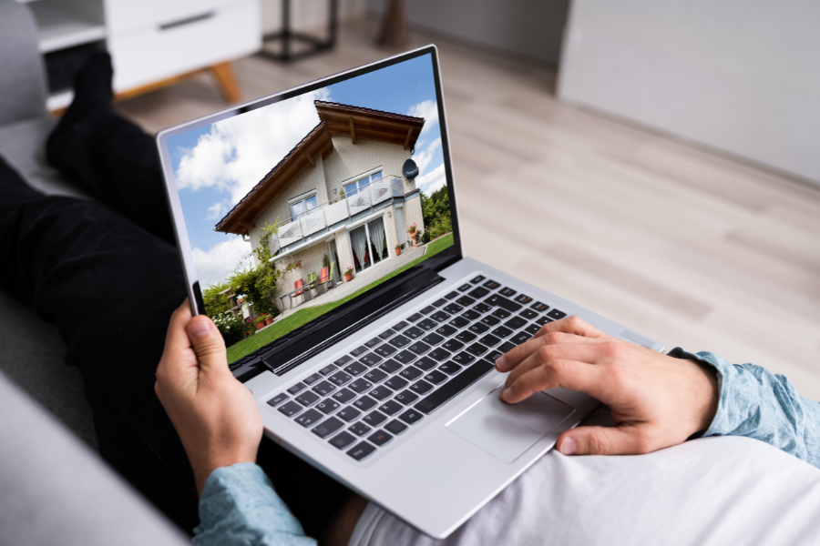 Man laying with computer on his lap looking at homes. 