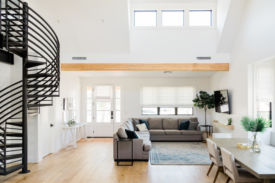 Open concept floor plan with black spiral staircase, gray sectional, and lots of natural light.