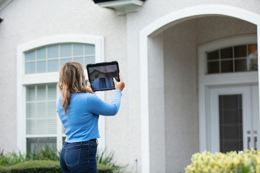 Professional in blue long sleeve shirt and jeans using tablet to take photos of beige home.