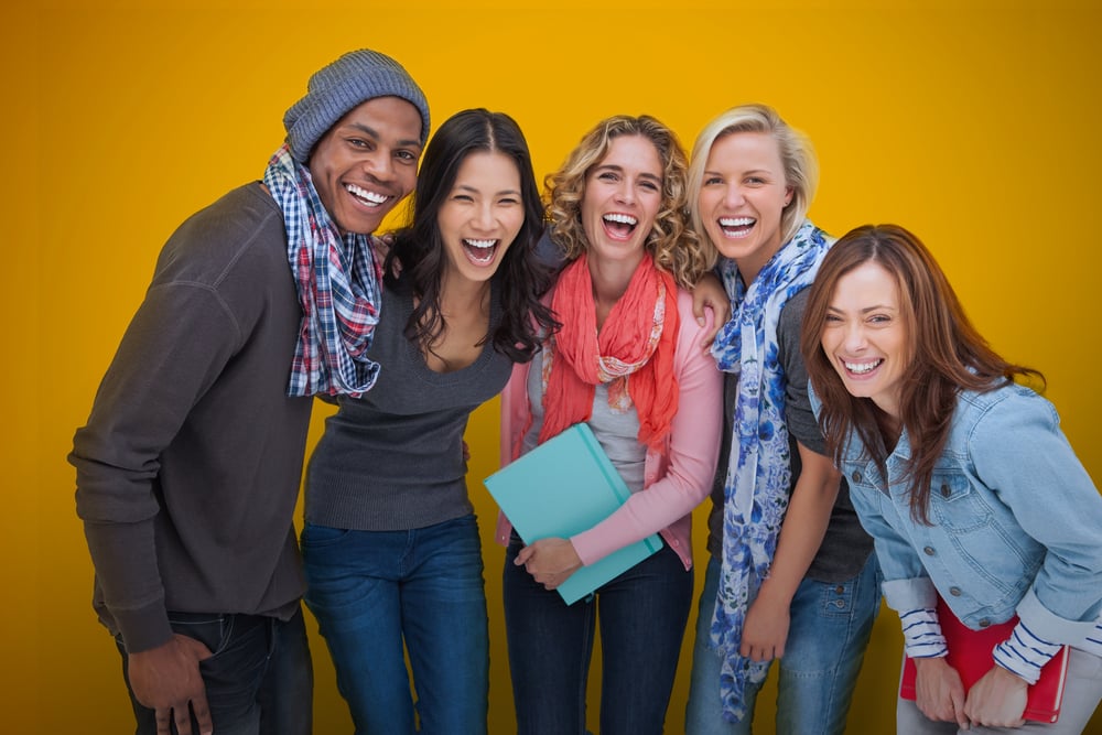 Cheerful group of friends laughing together on yellow background