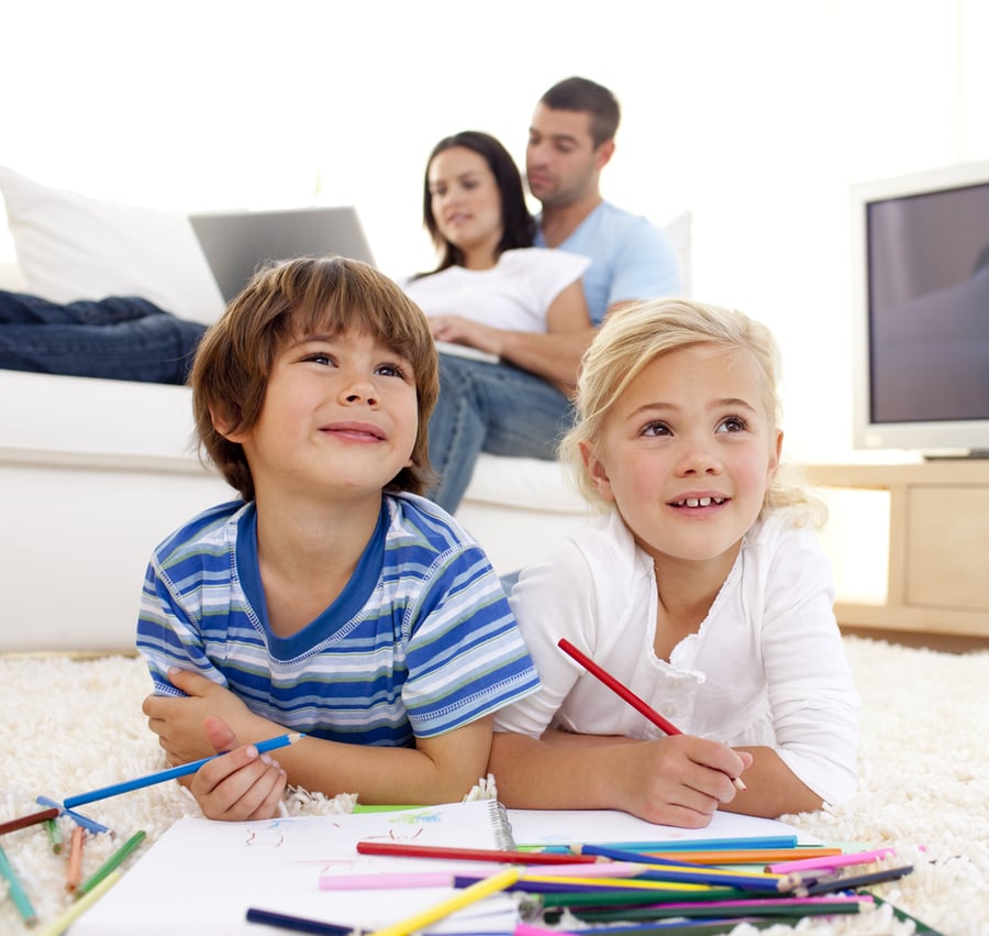 Children painting in living-room and parents using a laptop on sofa