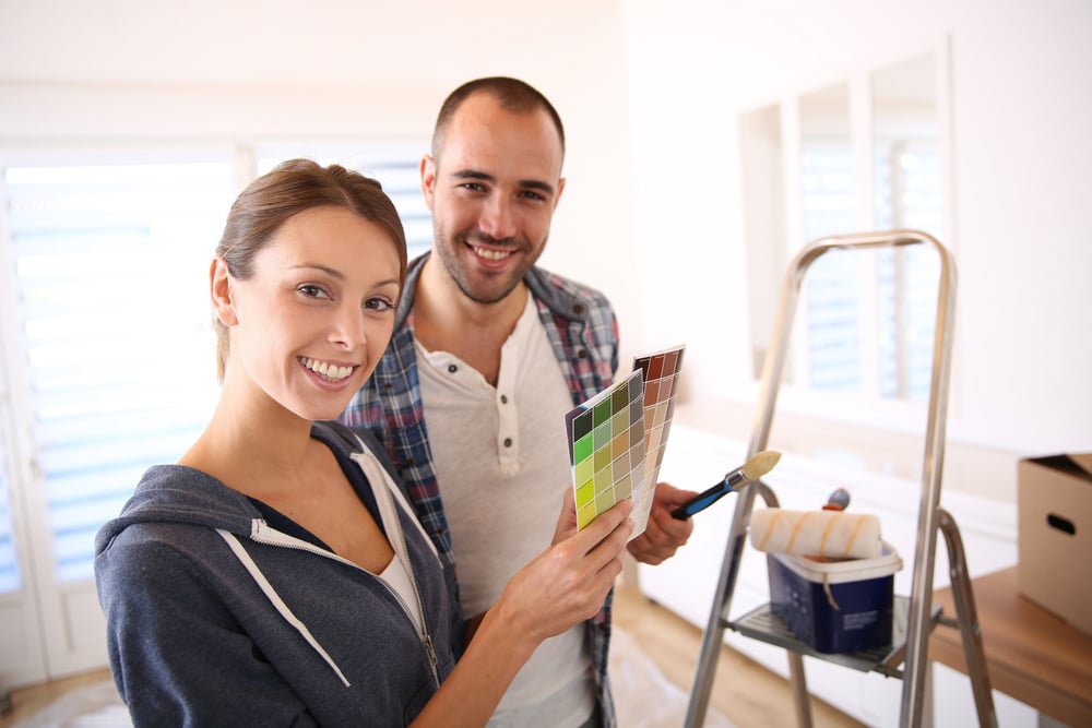 Couple in new house choosing color for walls from paint samples standing by ladders