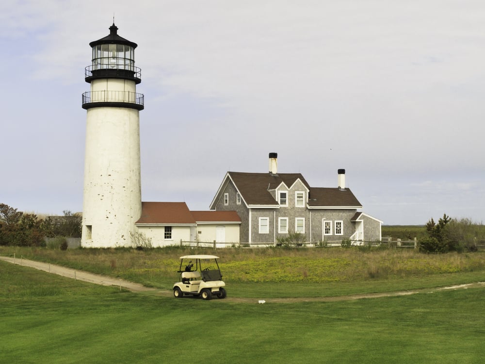 Golf cart on path around putting green by historic lighthouse and station in Cape Cod