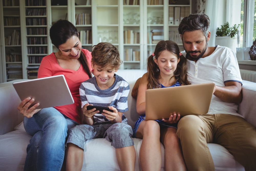 Happy family sitting on sofa and using laptop, mobile phone and digital tablet at home