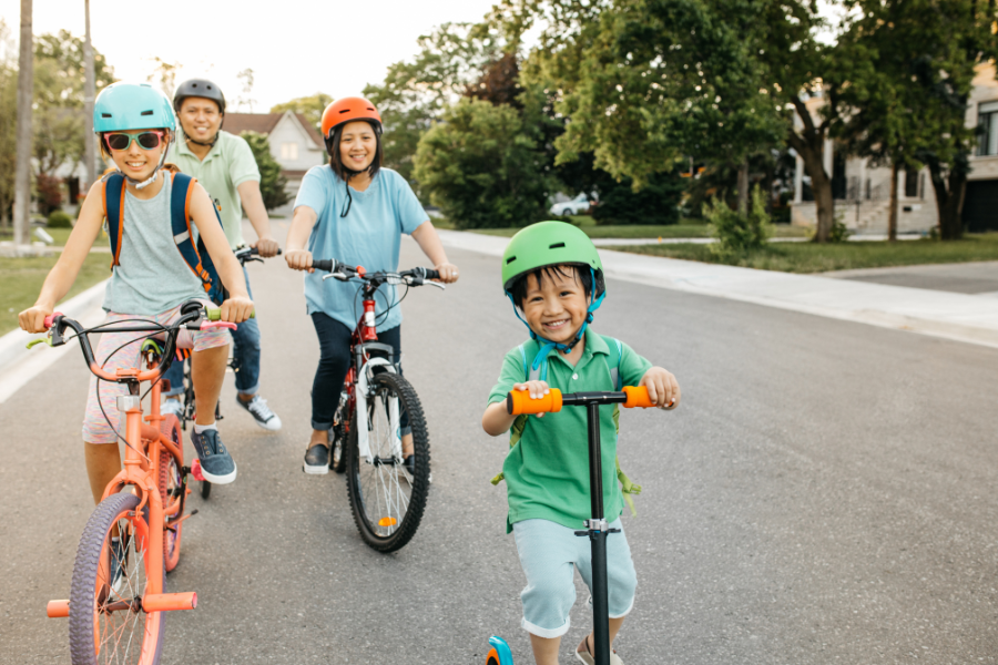 Family of four smiling and riding bikes through neighborhood in bright colors. 