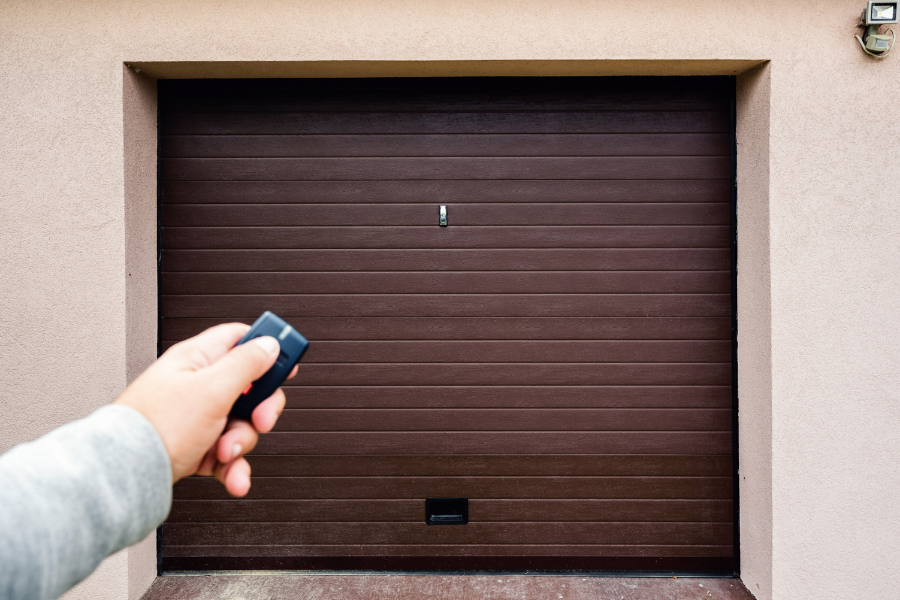 Person holding opener up to brown garage door. 