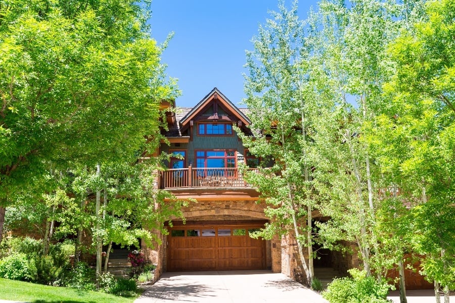 Rustic styled home with many trees and grown landscaping out front. 