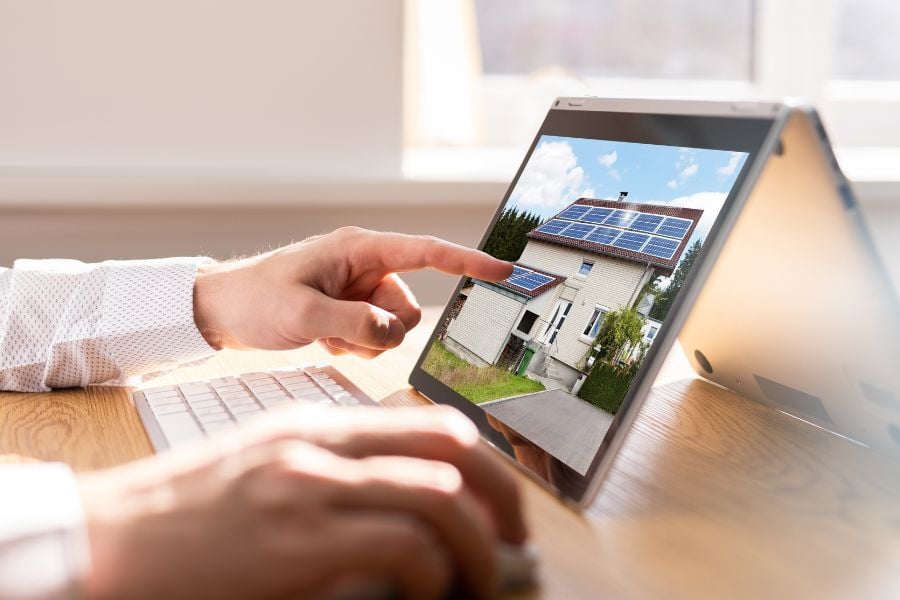 Man wearing white long sleeve points at real estate listing pulled up on tablet on table in front of him. 