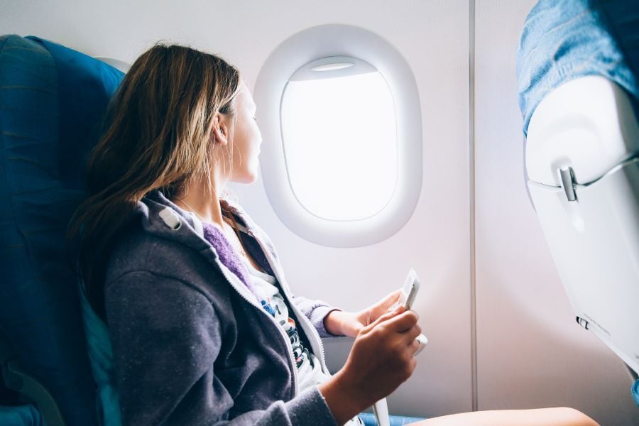 Woman gray hoodie sits in seat on airplane looks out window.