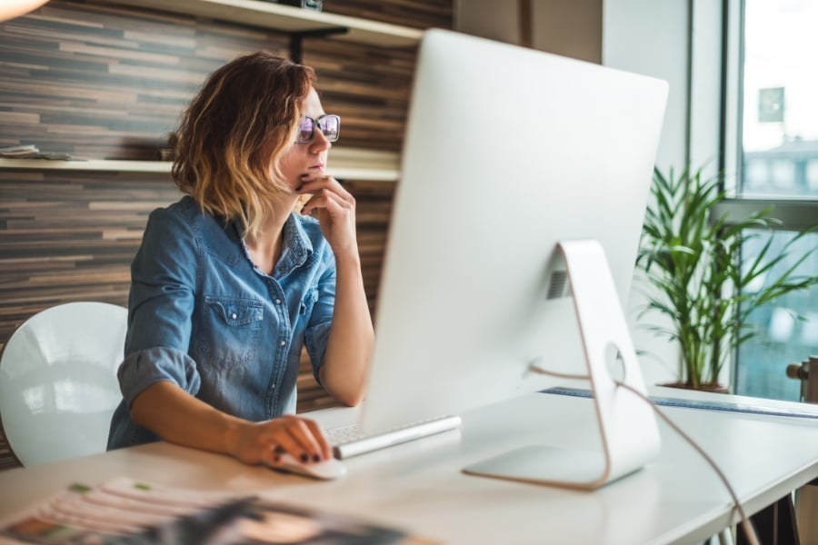 Woman in glasses and denim shirt virtually staging her home for sale on the computer. 