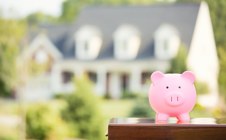 Pink piggy bank on a table in front of a blurred out home