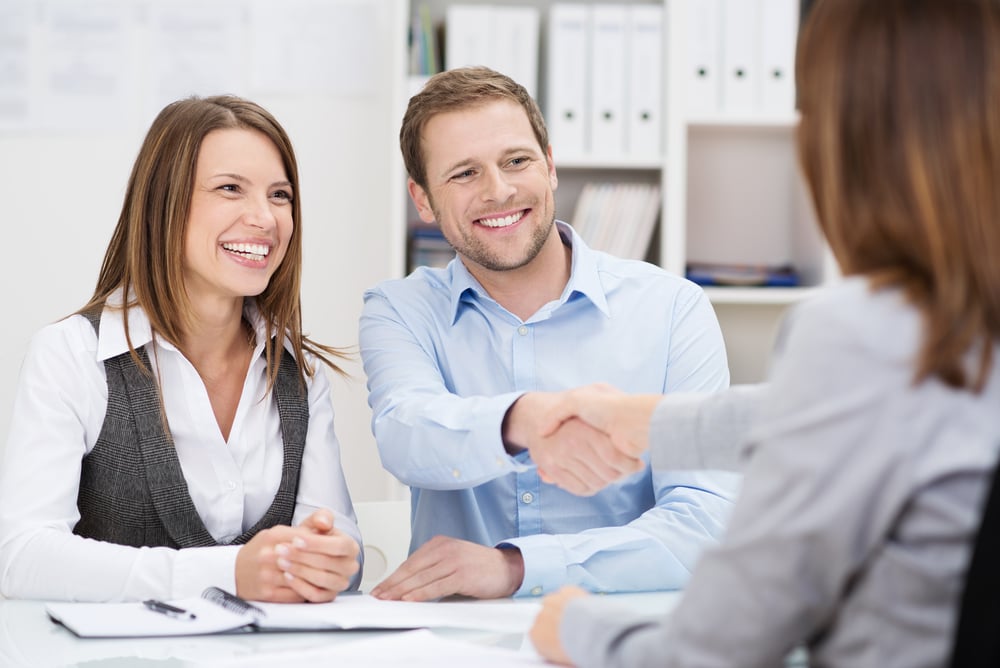 couple signing papers and shaking hands with closing agent