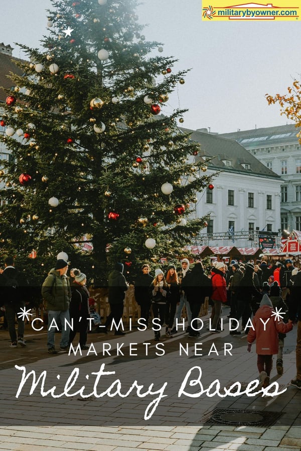 large crowd outside at town Christmas market with Christmas tree with ornaments and stalls selling holiday goodies near white buildings and textCant Miss Holiday Markets Near Military Bases