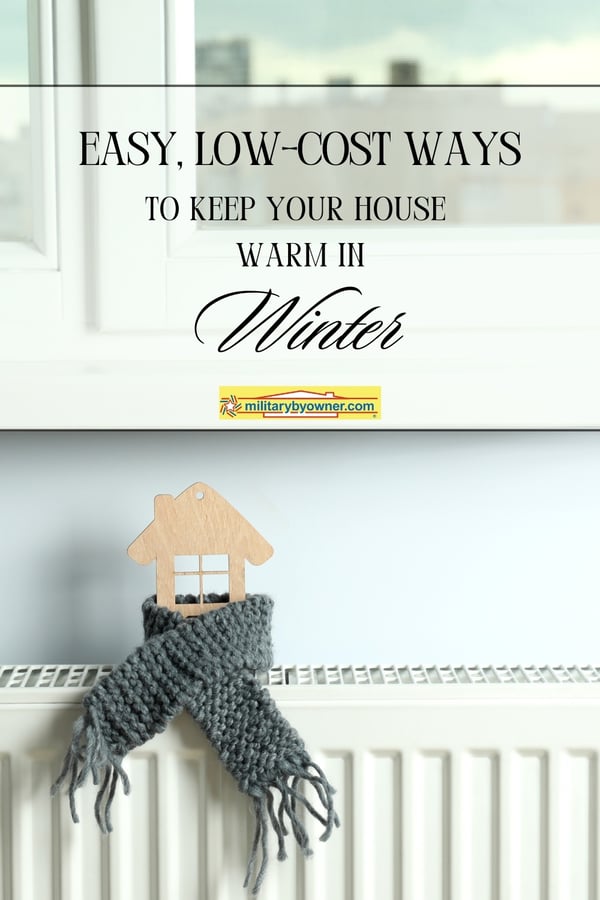 Photo of wooden 2D house sitting on white heater with a gray scarf wrapped around it with text, Easy Ways to Keep Your House Warm in Winter (Pinterest Pin)