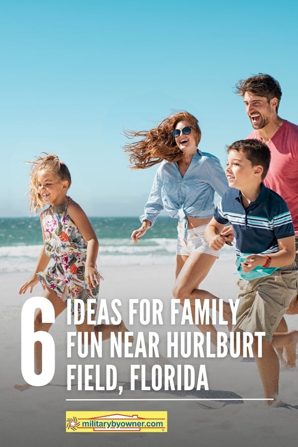 Family of four wearing bright colored summer clothes with hair blowing in the wind playfully run across white sandy beach with emerald water beside with text, 6 Ideas for Family Fun Near Hurlburt Field, Florida