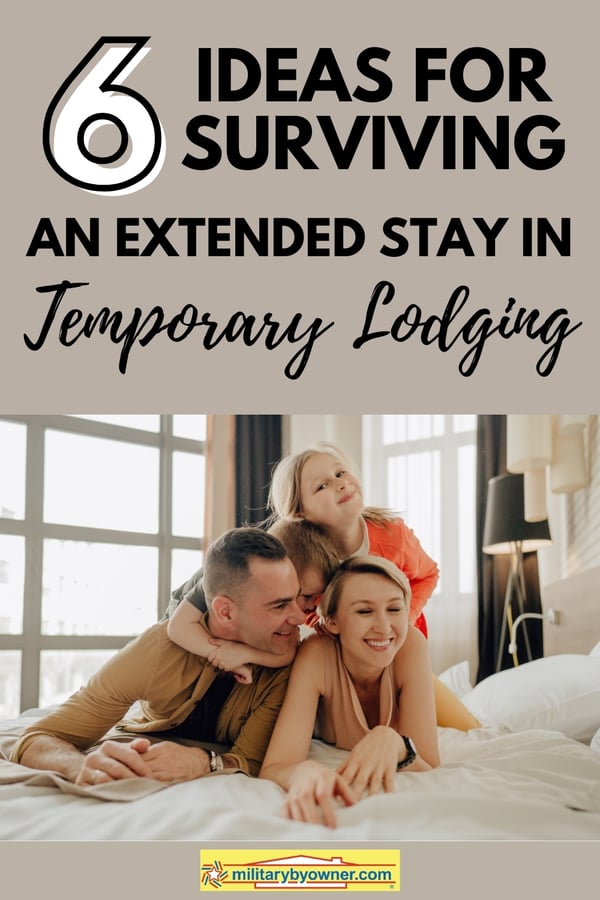 Two kids grabbing onto smiling mom and day who are laying propped up on their elbows on white bed in hotel room with text, 6 Ideas for Surviving an Extended Stay in Temporary Lodging