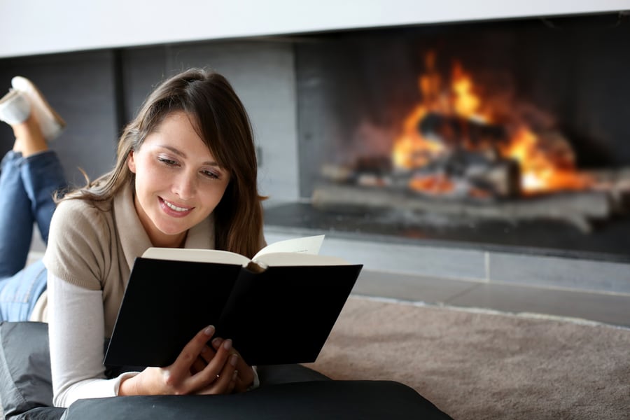 Woman reading book in front of fireplace