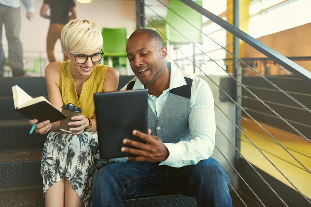 Two creative millenial small business owners working on social media strategy using a digital tablet while sitting in staircase-2