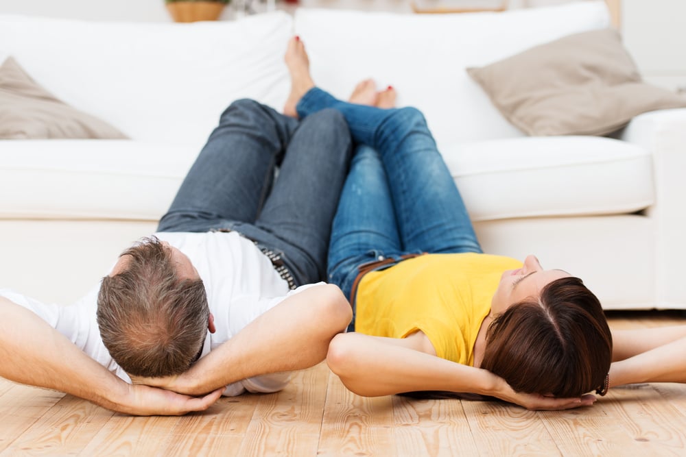 Young couple sharing a relaxing day lying side by side on their backs on a wooden living room floor with their bare feet up on the sofa