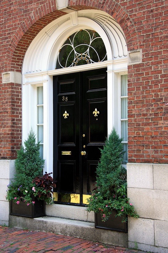 red brick home with black door and green potted plants