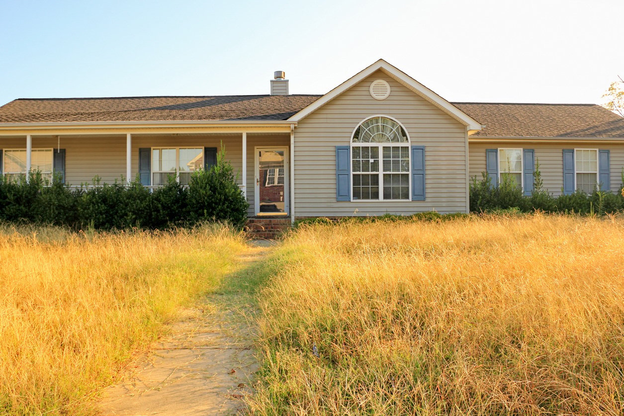 tan home in disrepair with overgrown lawn