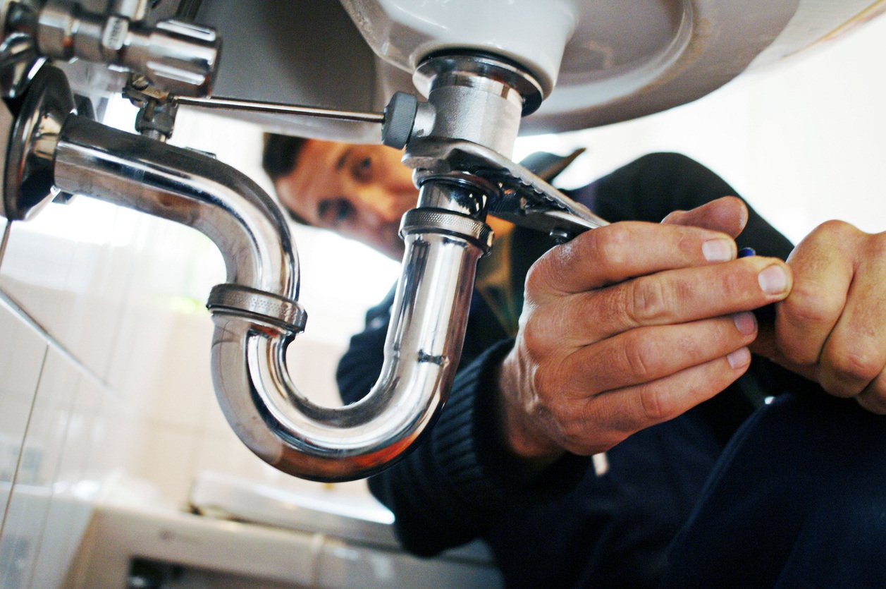 man fixing pipe under sink with wrench