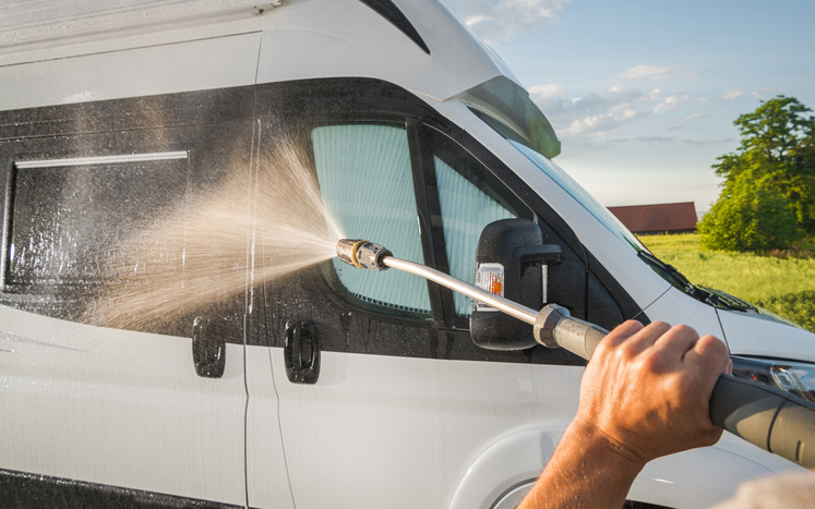 person cleaning RV with hose