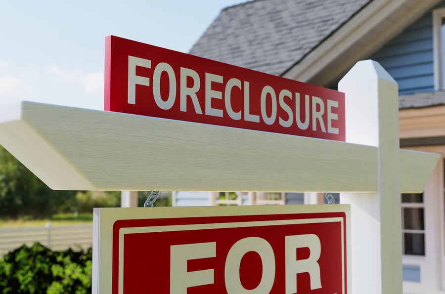 home in background with white and red sign that says foreclosure