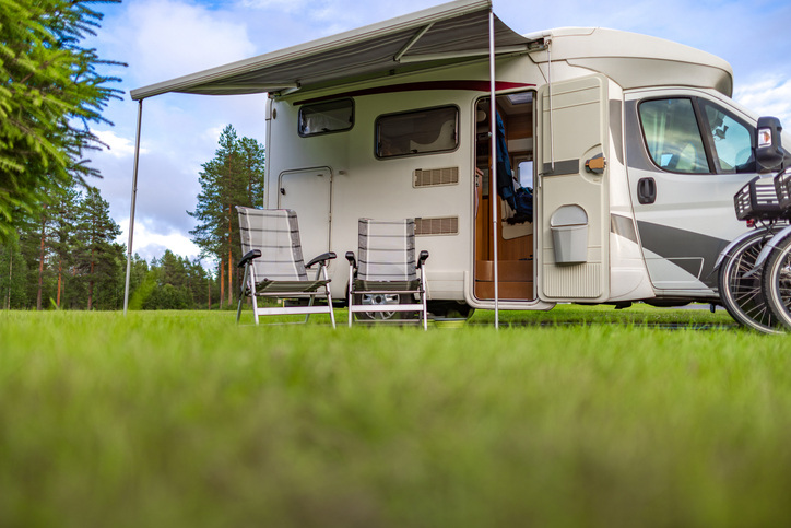 RV parked on grass with shade and chairs