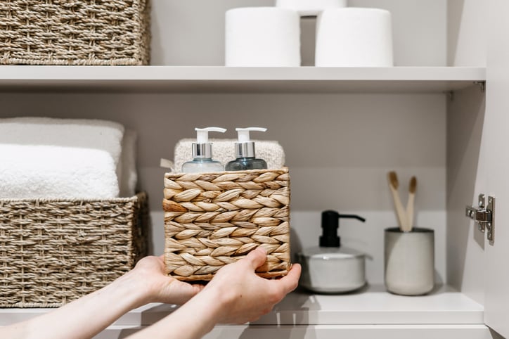 woman putting wicker basket on shelf in bathroom