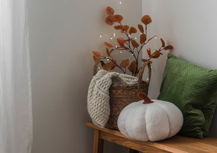 Cozy autumn decor interior concept. A basket with a blanket, a pillow, a pumpkin on a wooden bench