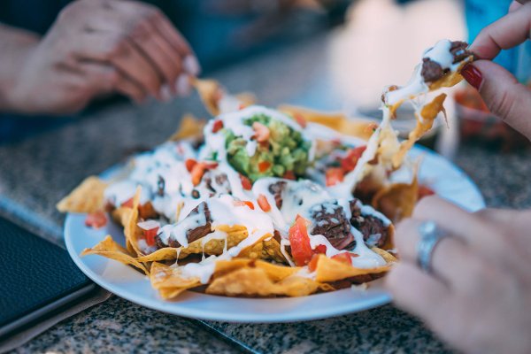 several people eating steak nachos off plate