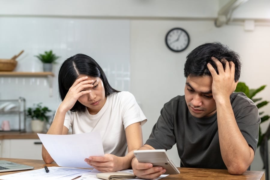 Photo of man and woman with hands in their hair concentrating on calculator and paper in front of them. 