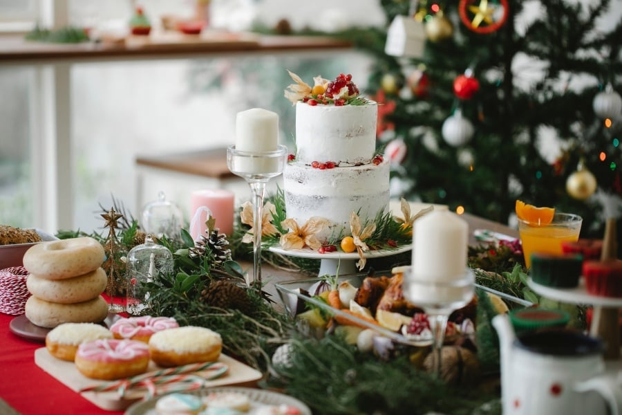 Holiday food including a two-tier white cake, candles and donuts with christmas tree and garland and pine cones 