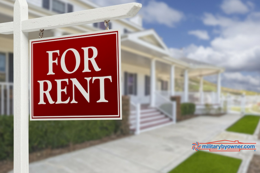 Photo of a rent and white For Rent sign in front of sidewalk with a white house with stairs in background.