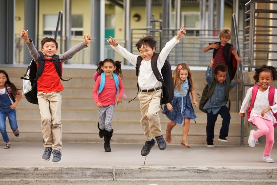 Photo of kids wearing backpacks running and jumping out of school doors down after school. 