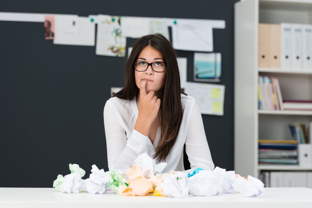 woman with hand on chin and looking up, thinking, with papers in front of her