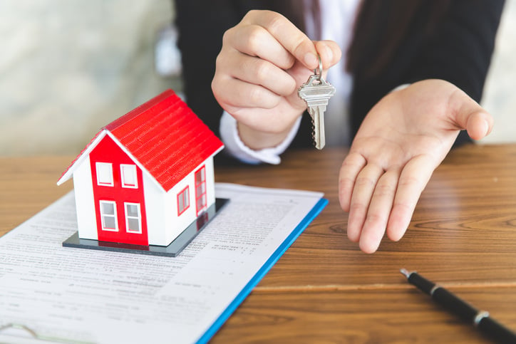 small model of home with person holding out hands and house key